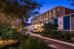 Un hotel moderno con varios pisos, iluminación exterior y un jardín paisajístico.