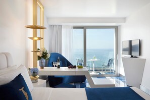 Una habitación de hotel moderna con una cama, un escritorio con un florero, una silla, un televisor y un balcón con vistas al mar.