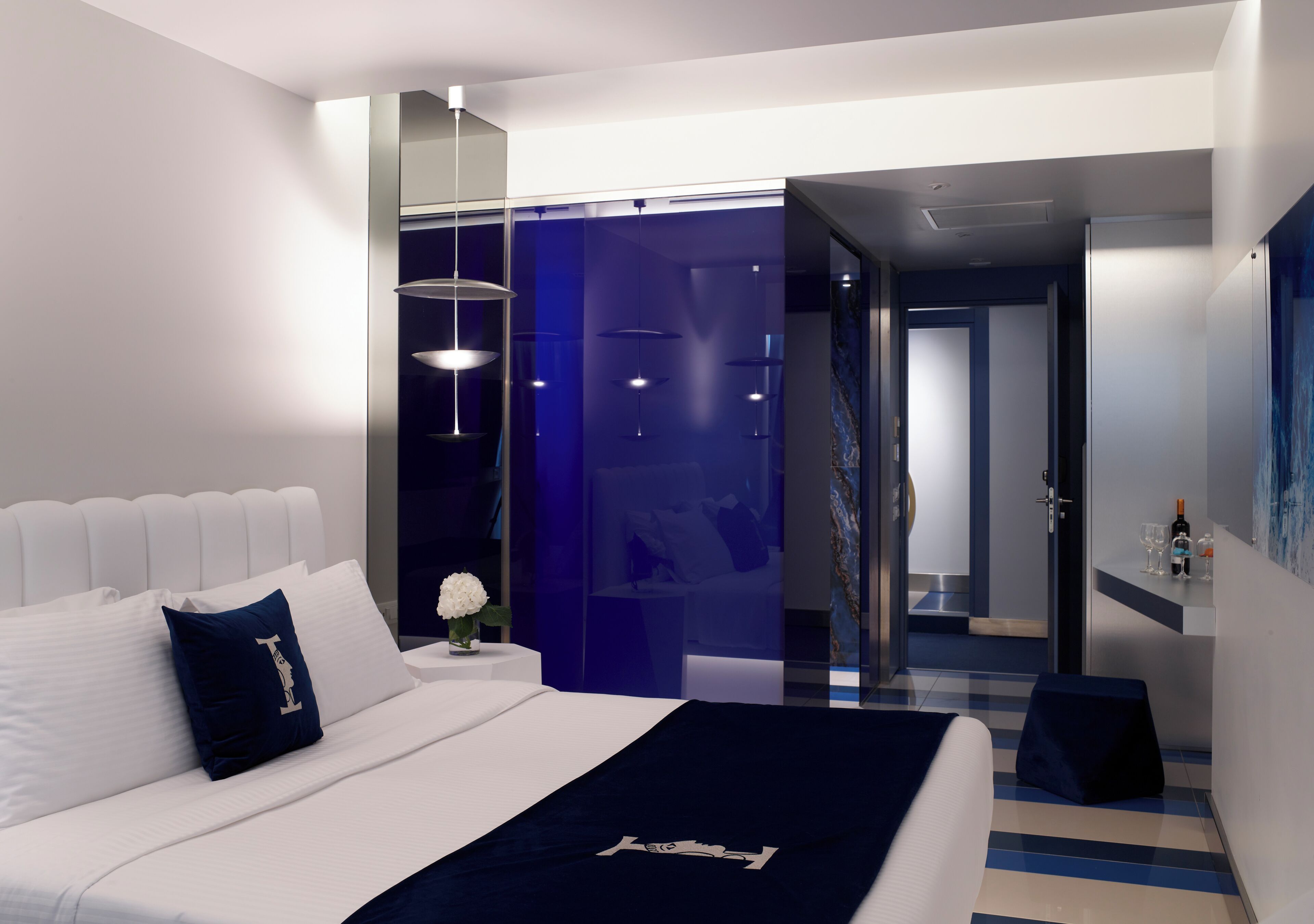 A modern hotel room with a large bed, a bedside table with a vase of flowers, and a view of the hallway.