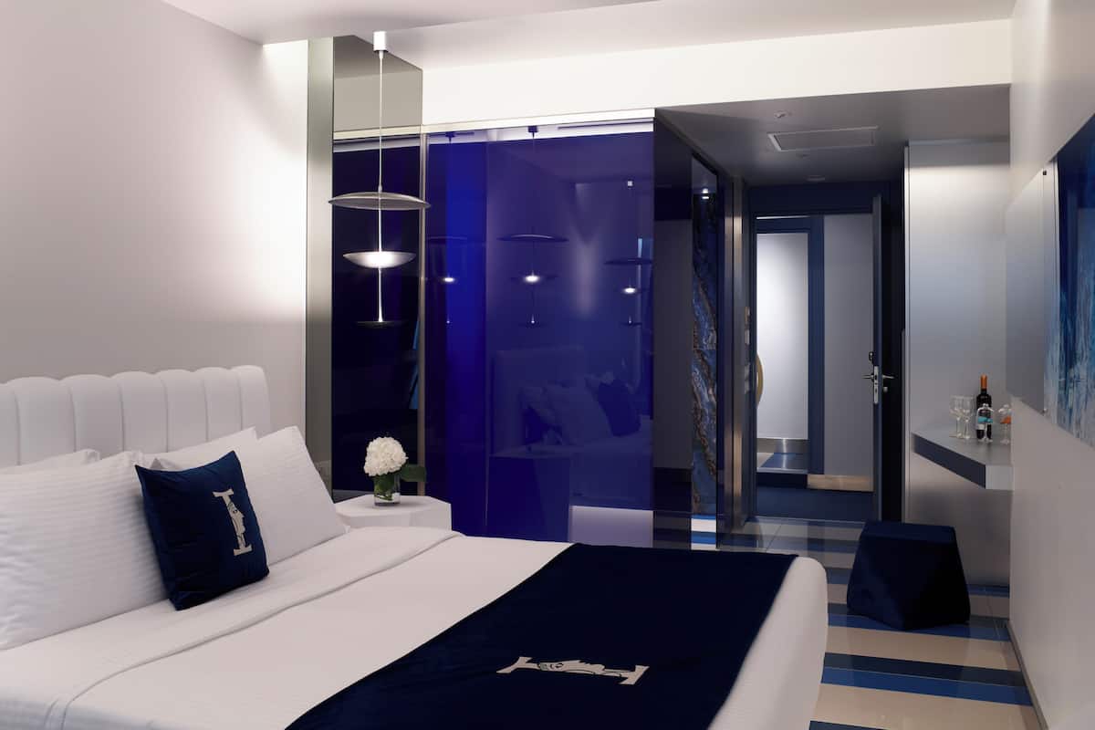 A modern hotel room with a large bed, a bedside table with a vase of flowers, and a view of the hallway.