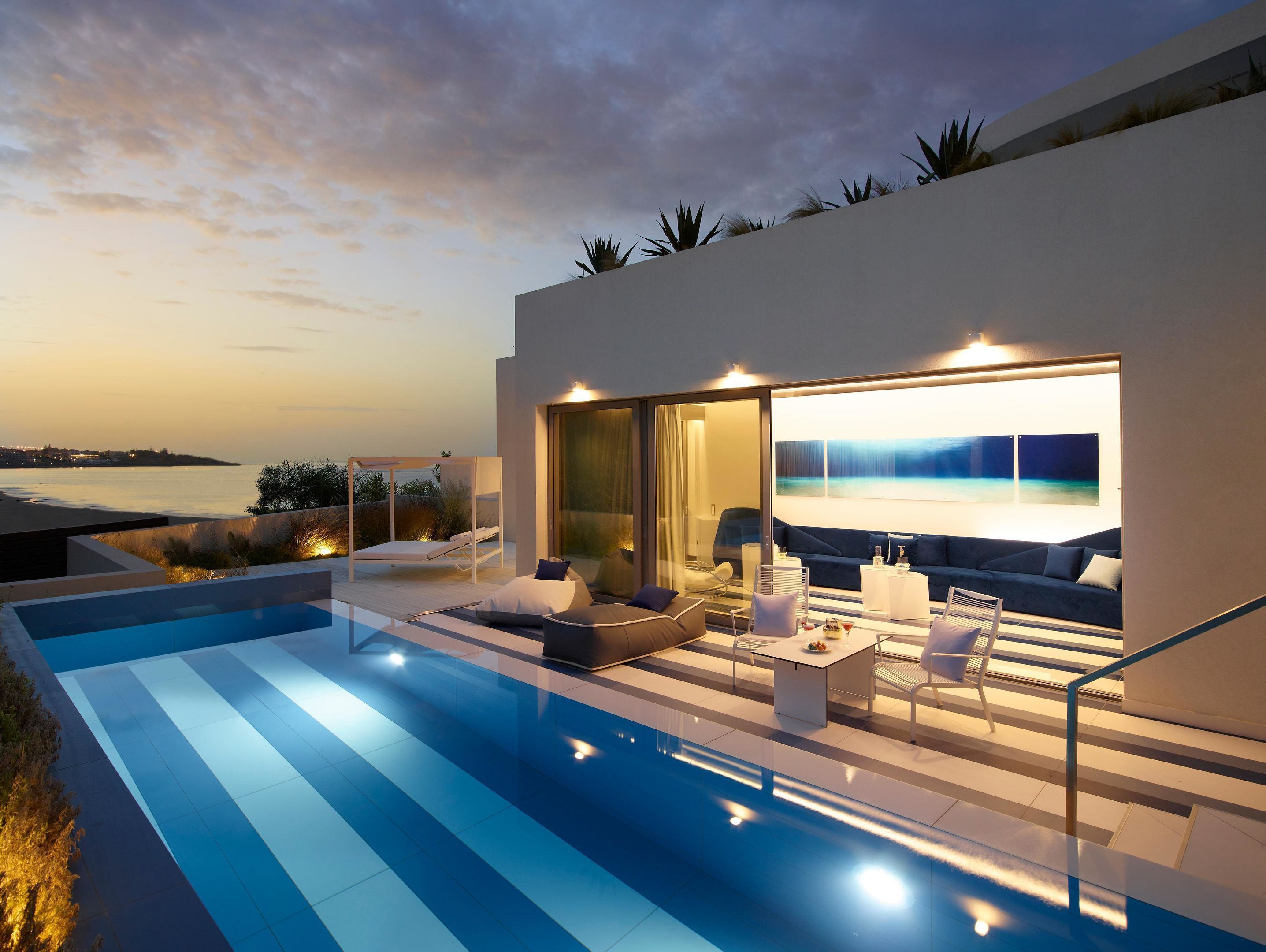 Ein moderner Außenbereich mit Pool, Sitzgelegenheiten und Blick auf das Meer im Dämmerlicht.