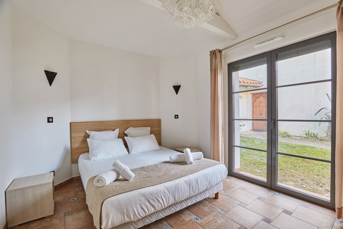 A bedroom with a large bed, a nightstand, and a sliding glass door to a courtyard.