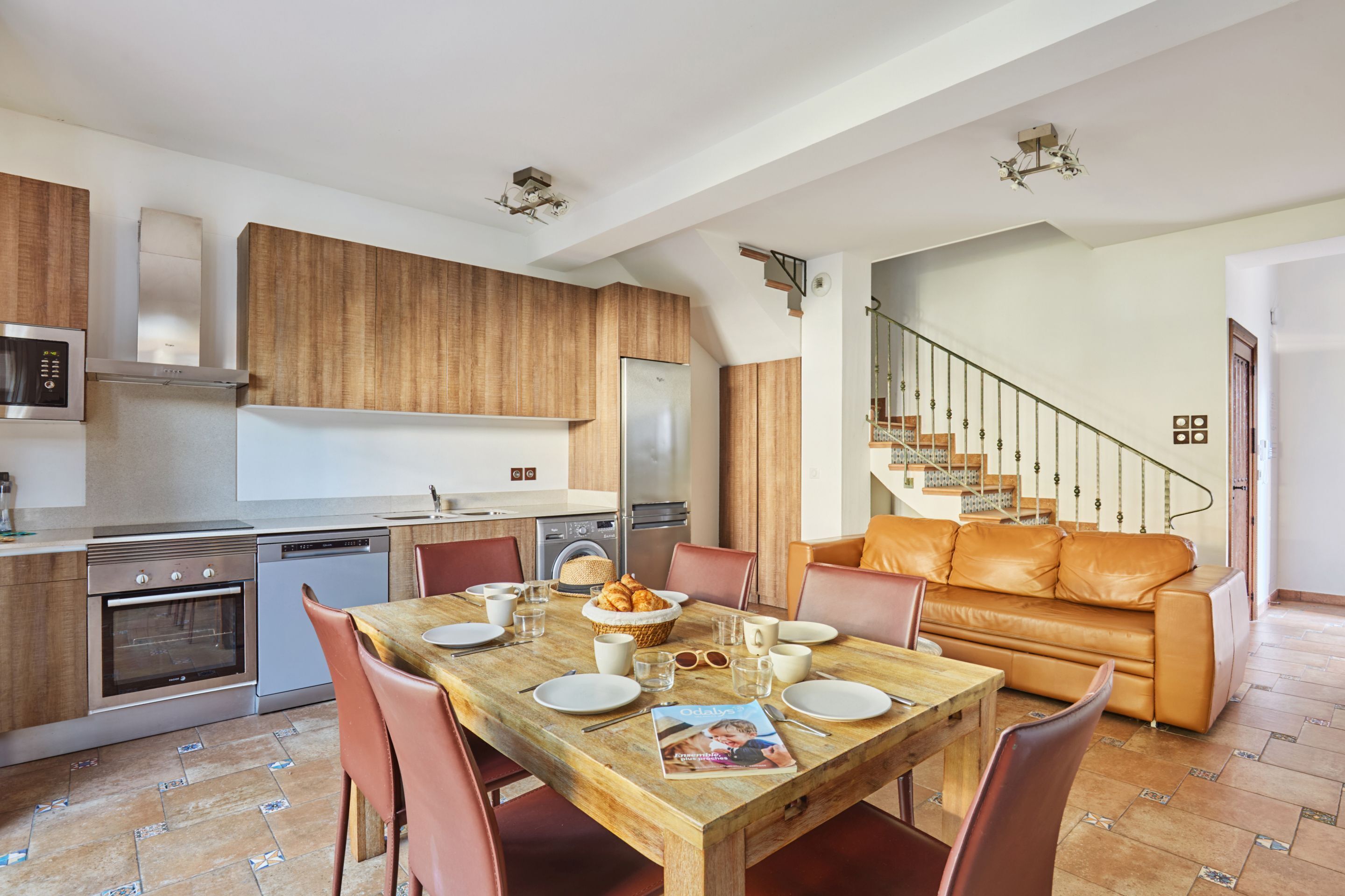 A modern kitchen with wooden cabinets, stainless steel appliances, and a dining area with a wooden table and leather chairs.