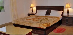 Una cama bien hecha con una colcha estampada de flores, dos lámparas de noche y una mesita en una habitación de hotel.