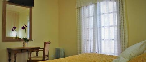 A bedroom with a bed, a desk, a chair, a radiator, and a window with curtains.