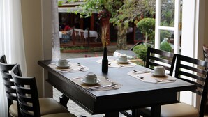 Une table à manger dressée avec des tasses et des soucoupes blanches, ainsi qu’un vase noir contenant des plantes séchées.