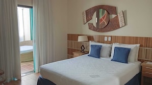 A hotel room with a large bed, a wooden headboard, a nightstand with a lamp, and a view of the outside balcony. - Summit Lago Hotel (Lambari)