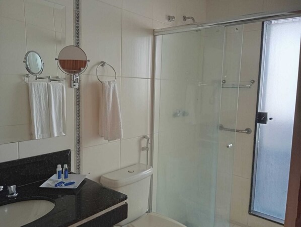 A bathroom with a toilet, a sink with toiletries, a mirror, and a glass-enclosed shower. - Summit Lago Hotel (Lambari)