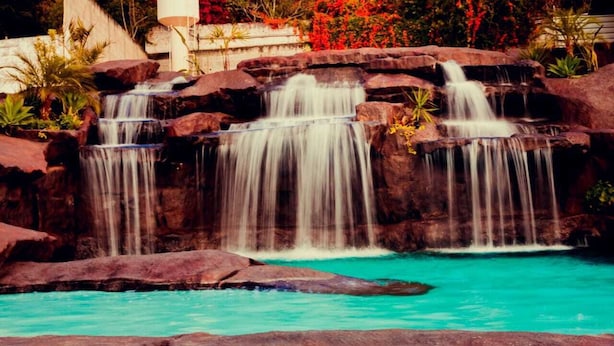 A waterfall cascading over rocks into a turquoise pool surrounded by large boulders and tropical plants. - Summit Lago Hotel (Lambari)