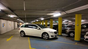 A multi-level underground parking garage with yellow pillars, marked parking spaces, and directional arrows on the floor.