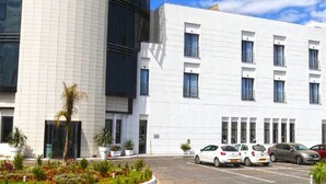A LE ZENITH HOTEL building with a modern design, featuring a prominent curved facade and a parking lot with several cars. - Le Zenith Hotel Oran (Oran)