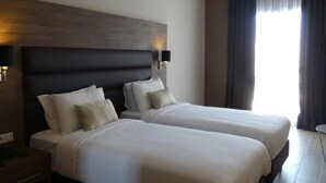 A hotel room with two beds, a dark headboard, bedside lamps, and a large window with curtains. - Le Zenith Hotel Oran (Oran)