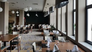 A modern restaurant with high ceilings, pendant lighting, and large windows. Tables are set with white tablecloths and napkins. - Le Zenith Hotel Oran (Oran)