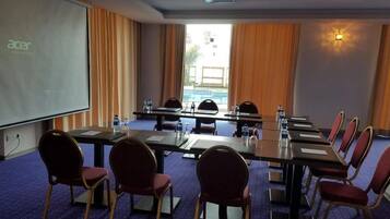 Un salón de conferencias con una larga mesa, sillas, una pantalla de proyector y vista a una piscina.