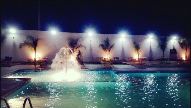 A nighttime pool area with a waterfall feature, surrounded by lounge chairs and tables under lighting. - Le Zenith Hotel Oran (Oran)