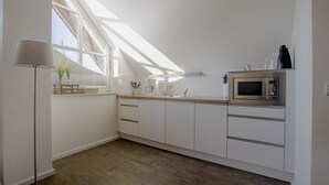A modern kitchen with white cabinets, a built-in microwave, and a skylight. - BUTZ home (Scharbeutz)