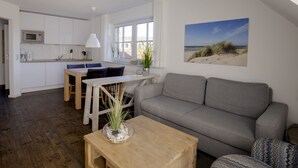 A modern living room with a grey sofa, wooden coffee table, and a dining area with a white table and chairs. - BUTZ home (Scharbeutz)