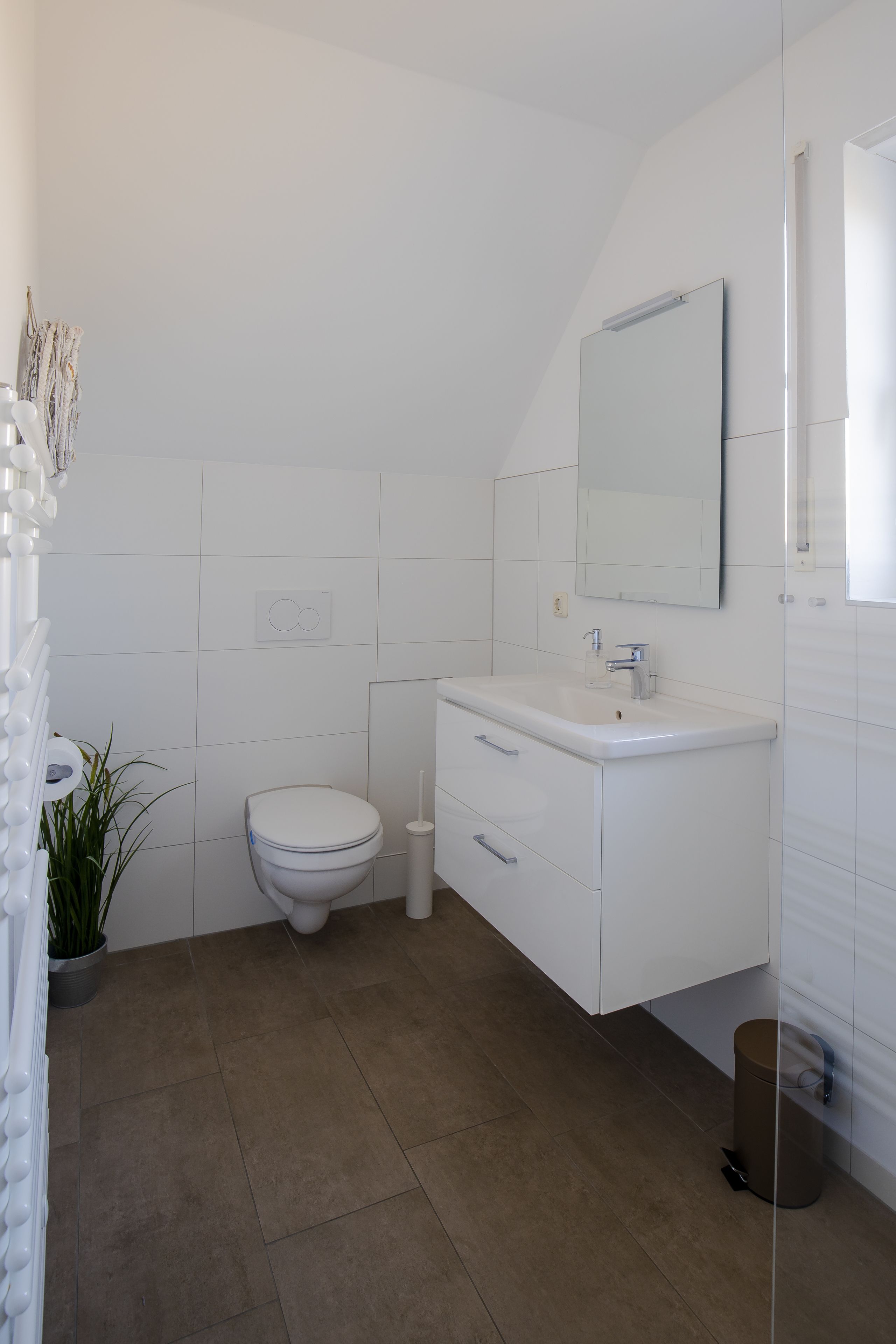 A modern bathroom with a white toilet, a sink with a mirror, and a potted plant.
