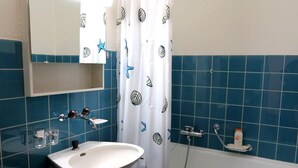 A bathroom with a white sink, blue tiled walls, a shower, and a mirror above the sink. - Popular and centrally located residential building in St. (St. Moritz)