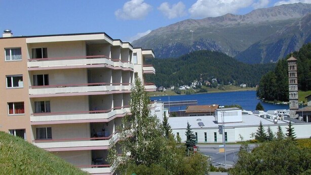 A multi-story building with balconies, a view of a lake, and mountains in the background. - Popular and centrally located residential building in St. (St. Moritz)