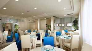 A restaurant with round tables, blue chairs, and white walls. - Hotel Turquoise (Cesenatico)
