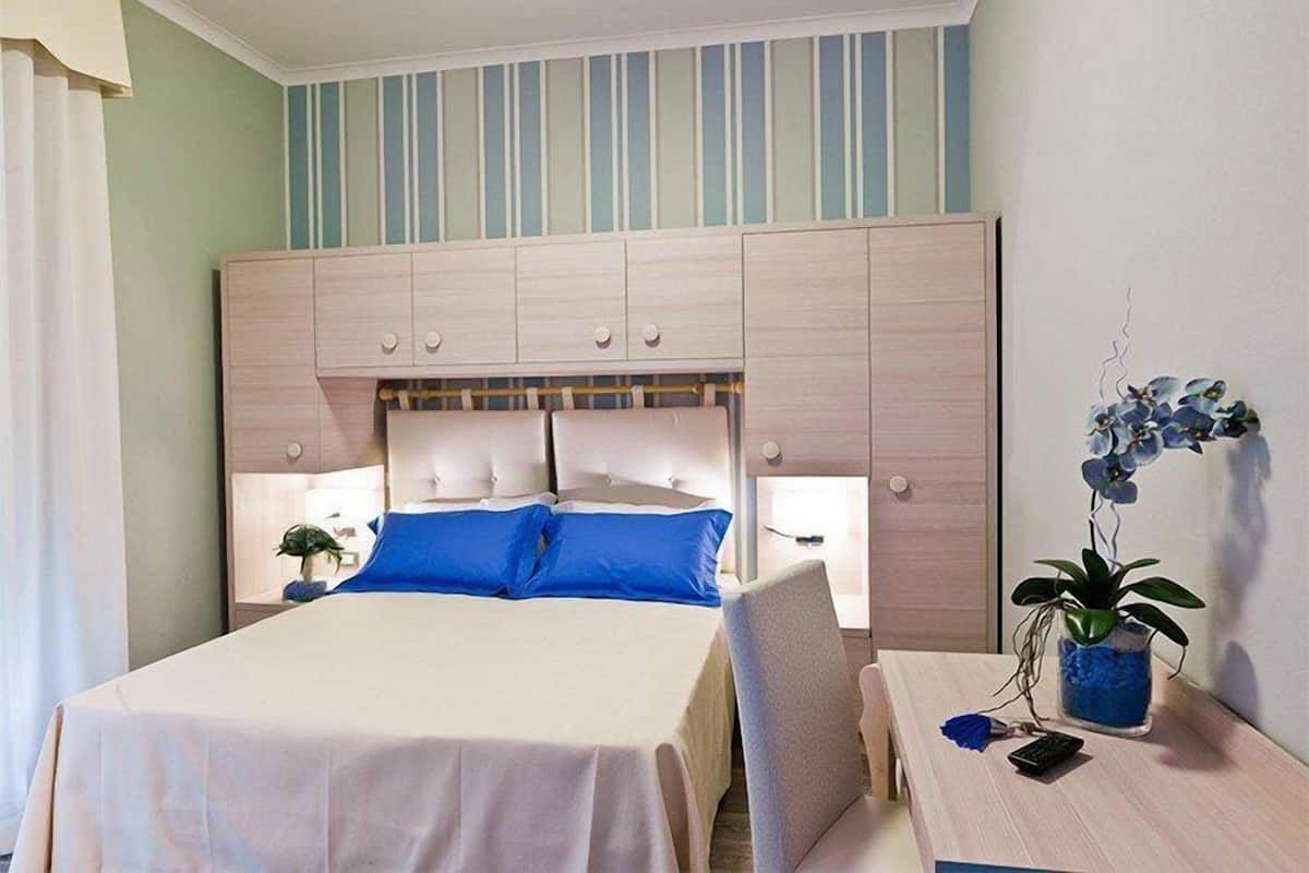 Une chambre d’hôtel avec un grand lit, une table de chevet avec une lampe, une chaise et une plante en pot.