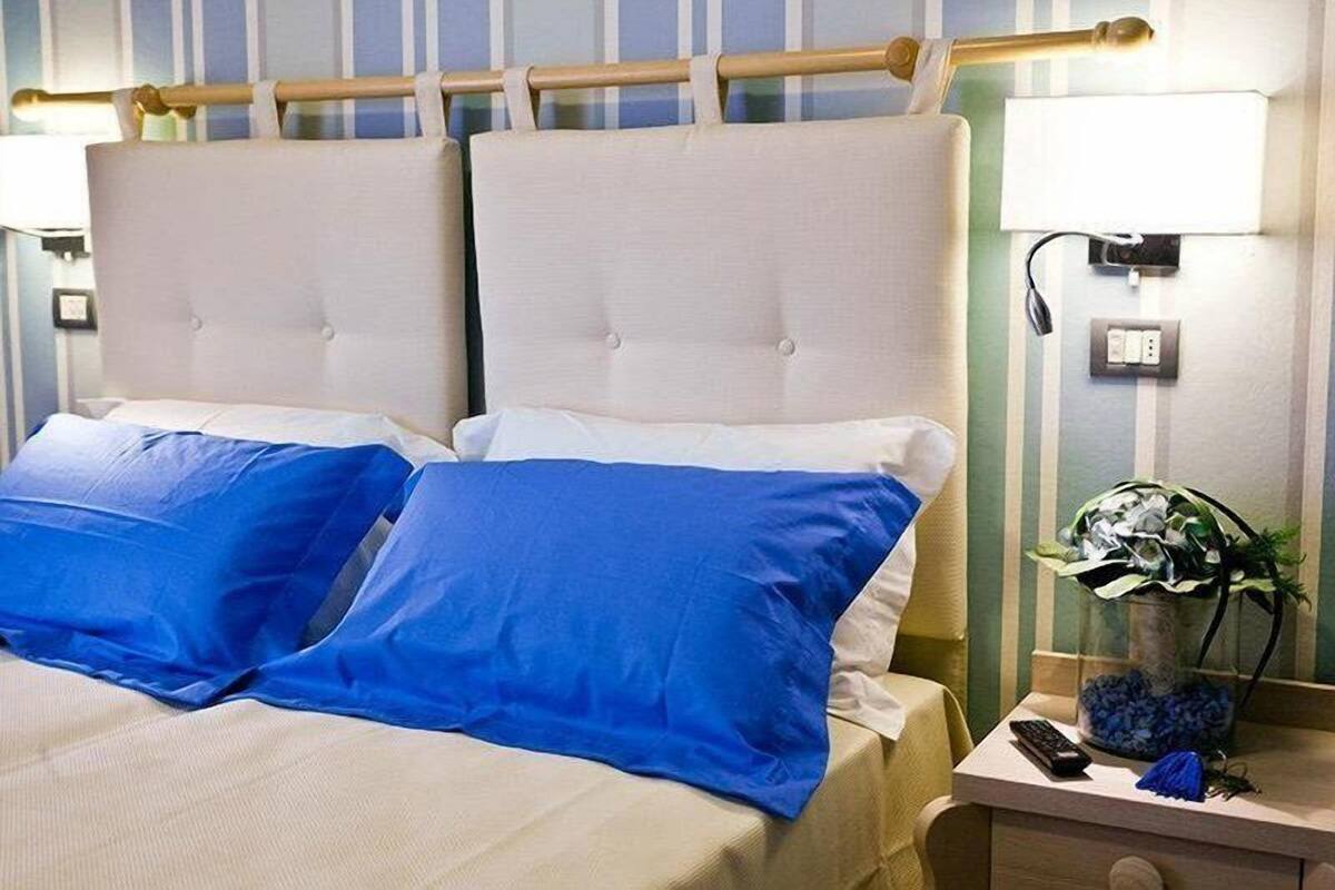 Un lit double avec deux oreillers bleus, une table de chevet avec une lampe, une télécommande et un vase avec des fleurs.
