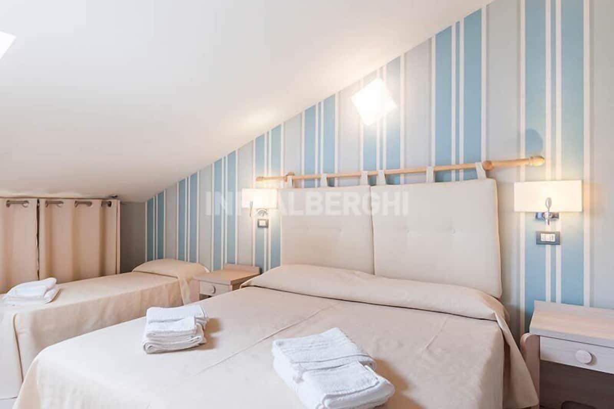 Une chambre d’hôtel avec deux lits, une grande fenêtre et un papier peint à rayures.