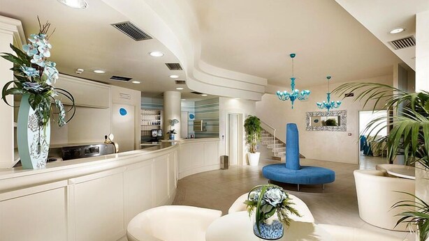 A modern hotel lobby with a curved reception desk, seating area, and decorative plants. - Hotel Turquoise (Cesenatico)