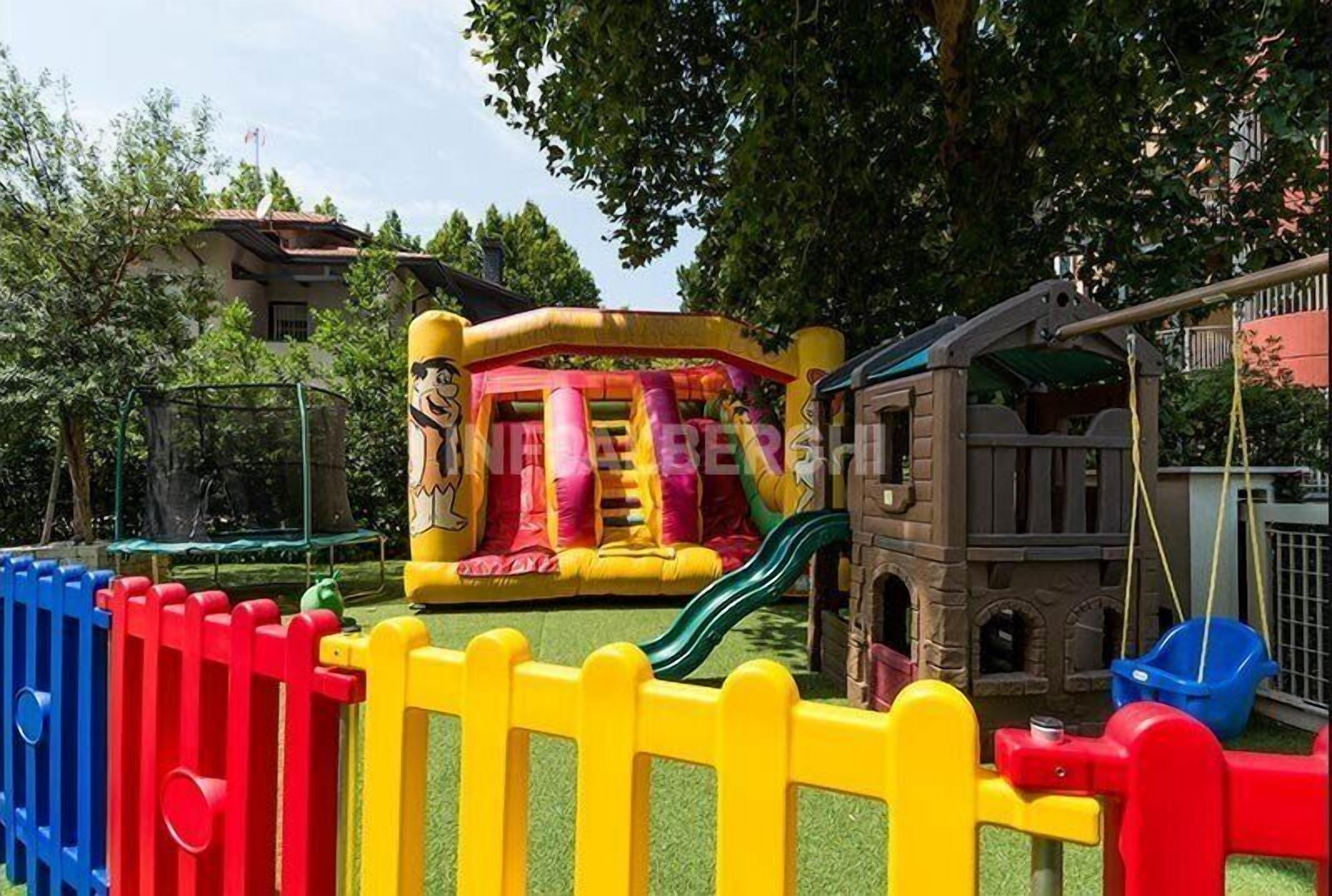 Un área de juegos infantiles con una estructura inflable de colores, un tobogán y un pequeño edificio.