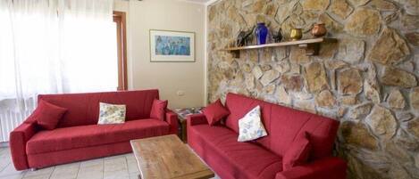 A living room with two red sofas, a wooden coffee table, a stone wall, and a shelf with decorative items.