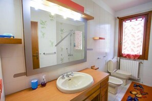 A bathroom with a large mirror, a sink, a toilet, and a shower. - Villa Serena (Portoferraio)