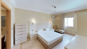 A bedroom with a large bed, a nightstand, a dresser, a chair, and a window. - Goldcity Holiday Homes (Alanya)