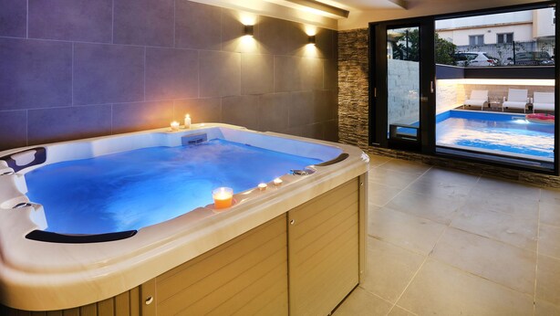 A hot tub with candles, a stone wall, and a view of a pool and building. - Villa M (Split)