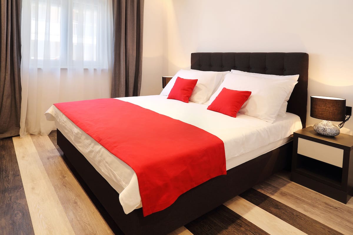 Un lit bien fait, avec une couvre-lit rouge et blanche, une tête de lit noire et une lampe de chevet.