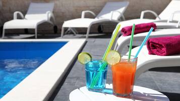 A poolside area with lounge chairs and two drinks with straws and lime slices.