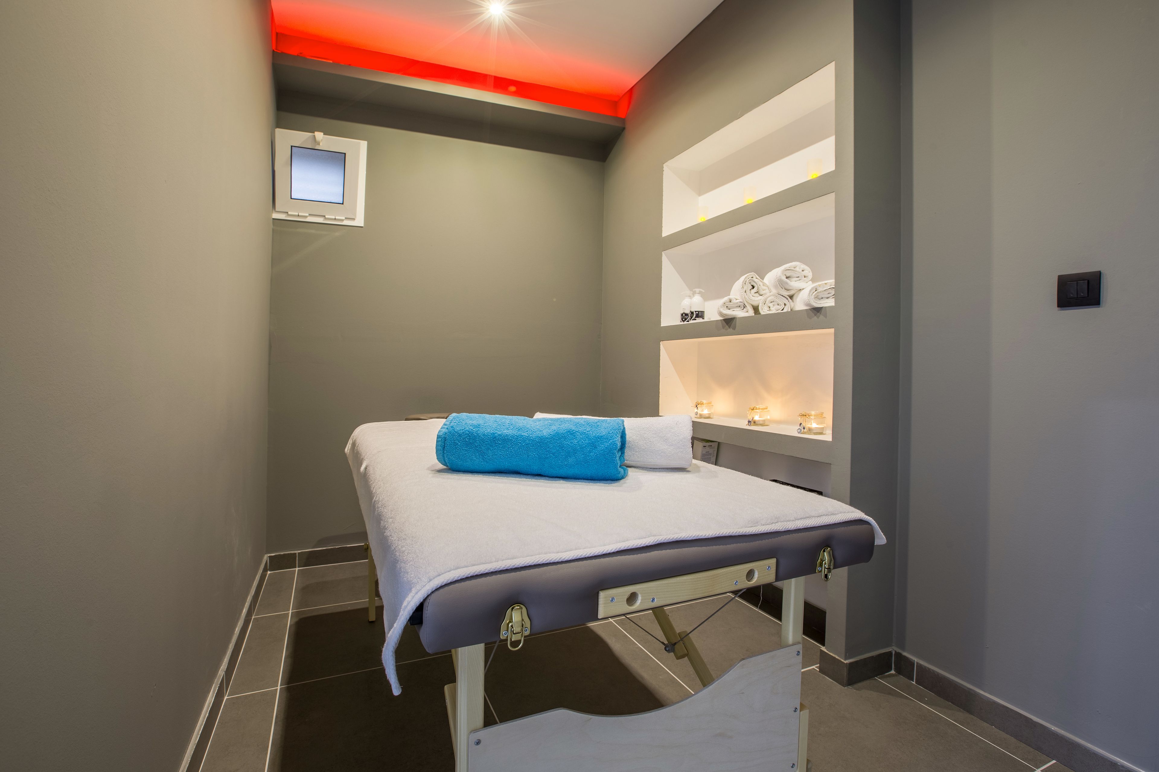 A treatment room with a bed, a small window, and shelves with towels.
