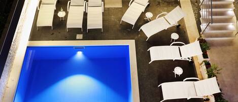 A rooftop pool area with multiple sun loungers and a central pool.