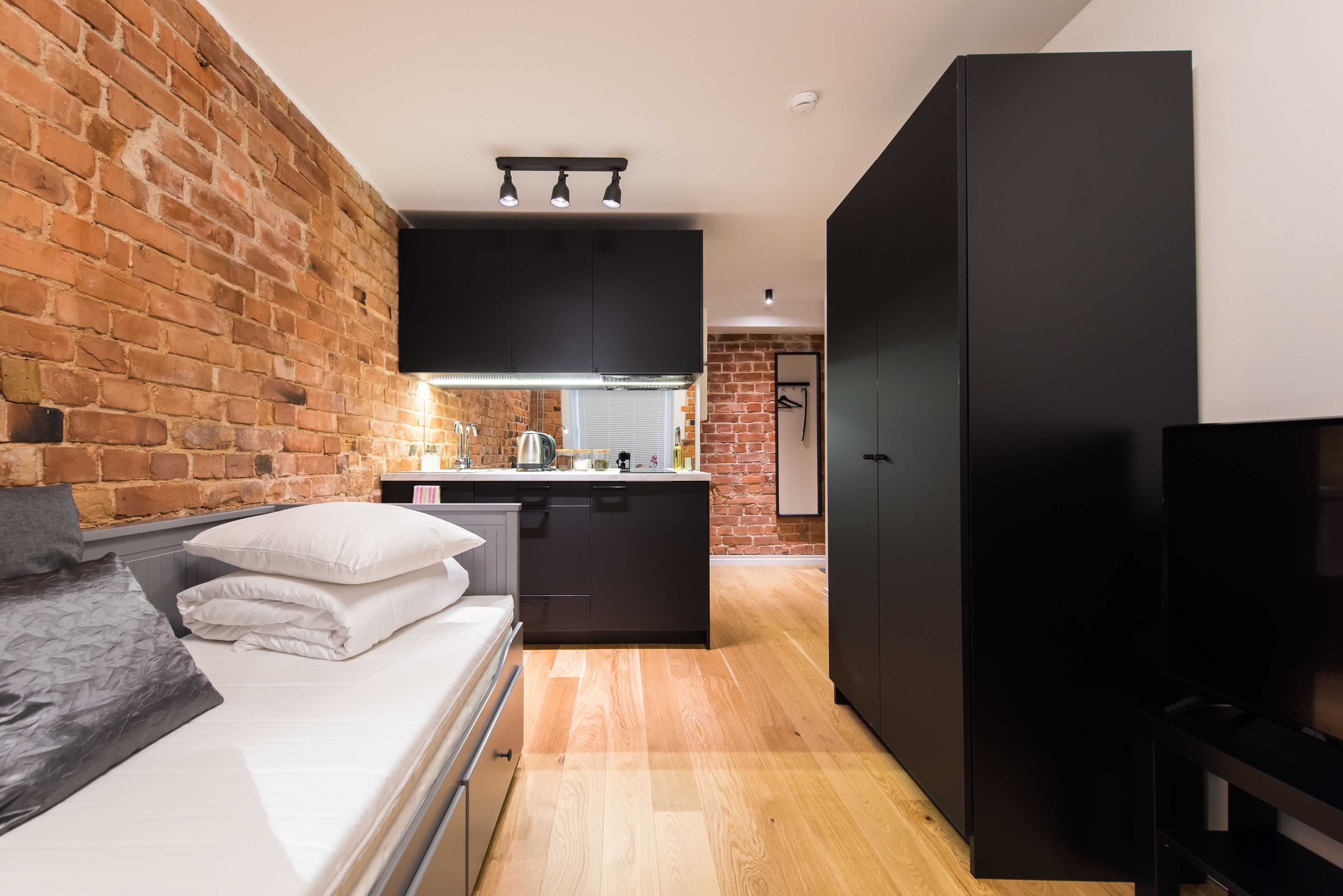 A compact bedroom with a bed, a small kitchenette, and a TV.