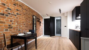 A modern kitchen with a brick wall, black cabinets, and a dining area with a table set for two. - Hilltop Apartments City Centre (Tallinn)