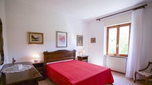 Une chambre à coucher avec un lit en bois, un bureau avec une lampe, une chaise et une fenêtre avec des rideaux.
