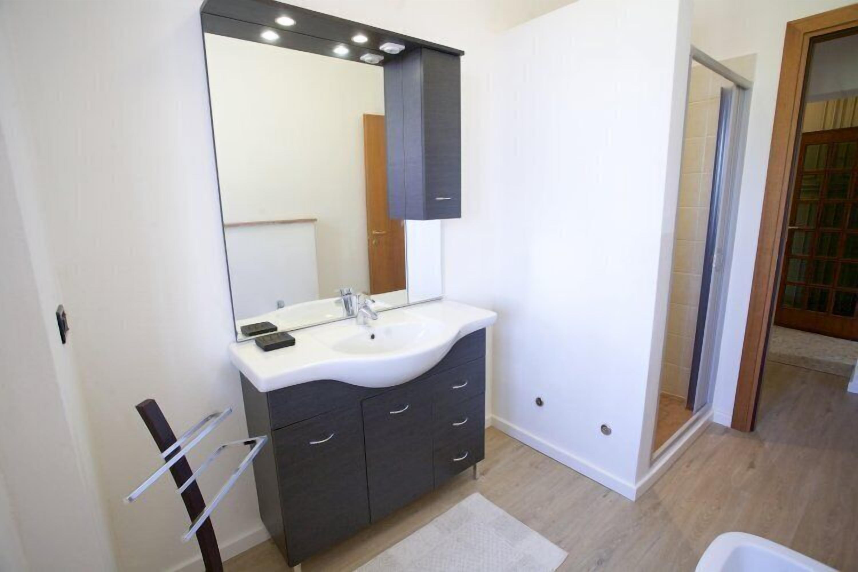 Un baño moderno con un lavamanos blanco, muebles oscuros y un espejo grande.
