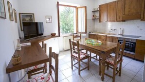 Une cuisine compacte avec des meubles en bois, une table à manger avec des chaises, un téléviseur et une fenêtre qui laisse entrer la lumière naturelle.