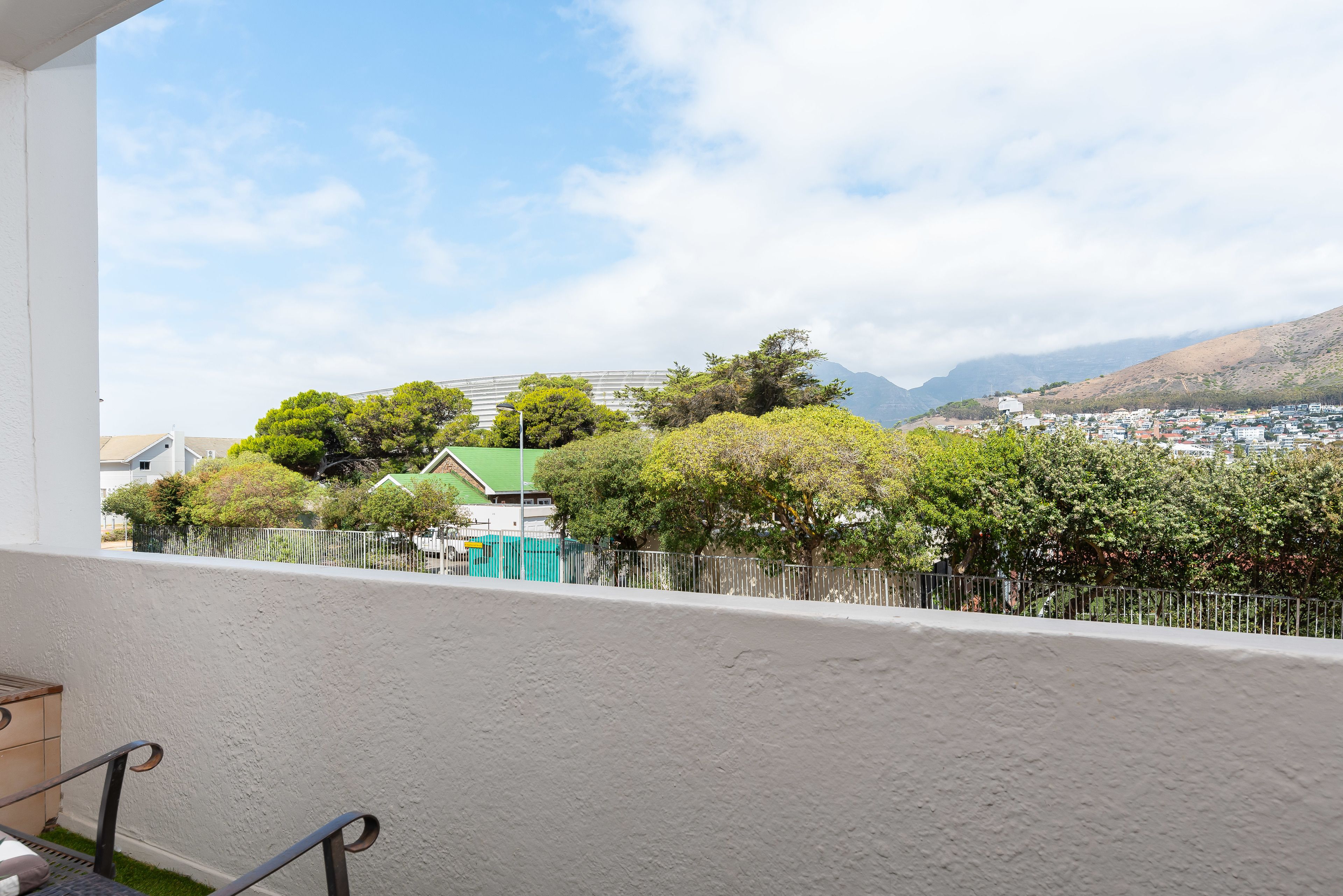 Un balcon donnant sur un quartier résidentiel, un immeuble doté d’un toit végétalisé et une montagne en arrière-plan.