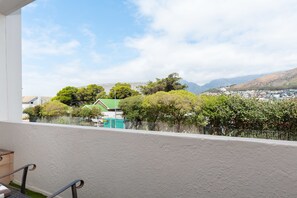 A balcony with a view of a residential area, a green-roofed building, and a mountain in the background. - Sandringham 23 (Cape Town)