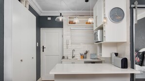 A modern kitchen with a white countertop, hanging pendant lights, a built-in oven, and a clock on the wall. - Sandringham 23 (Cape Town)