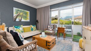 A living room with a sofa, chairs, a wooden coffee table, and a painting of a tree. - Sandringham 23 (Cape Town)