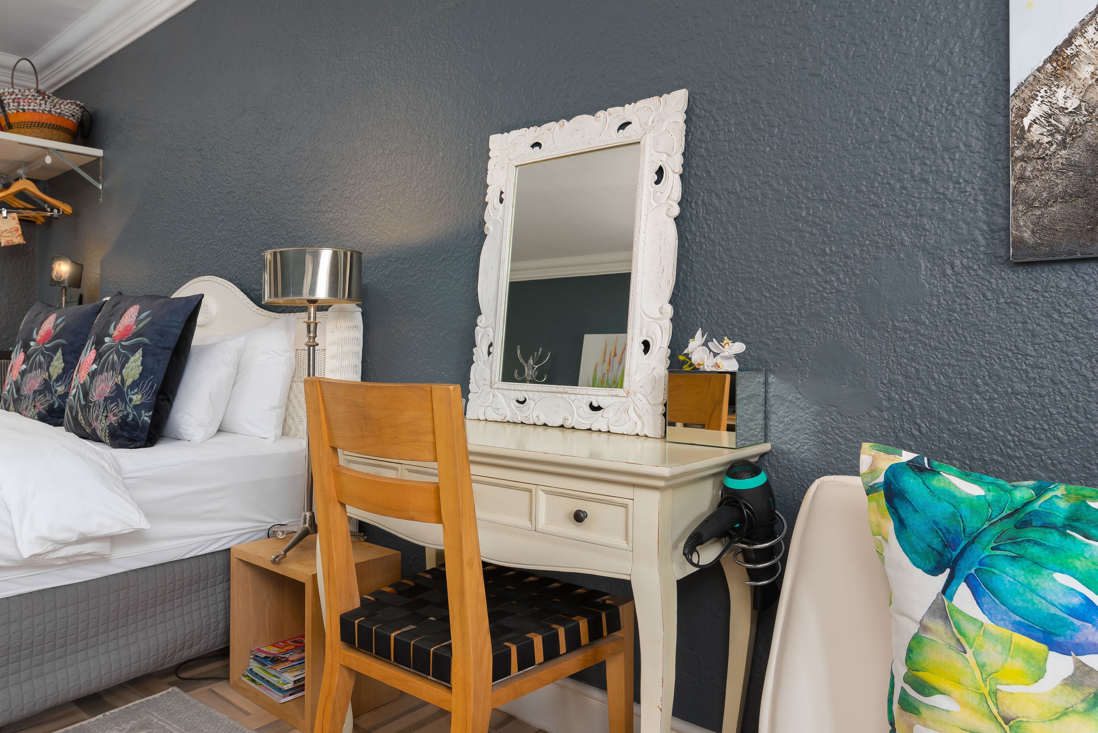 Un dormitorio con una cama, una silla de madera, un escritorio con un espejo y una mesita de noche.