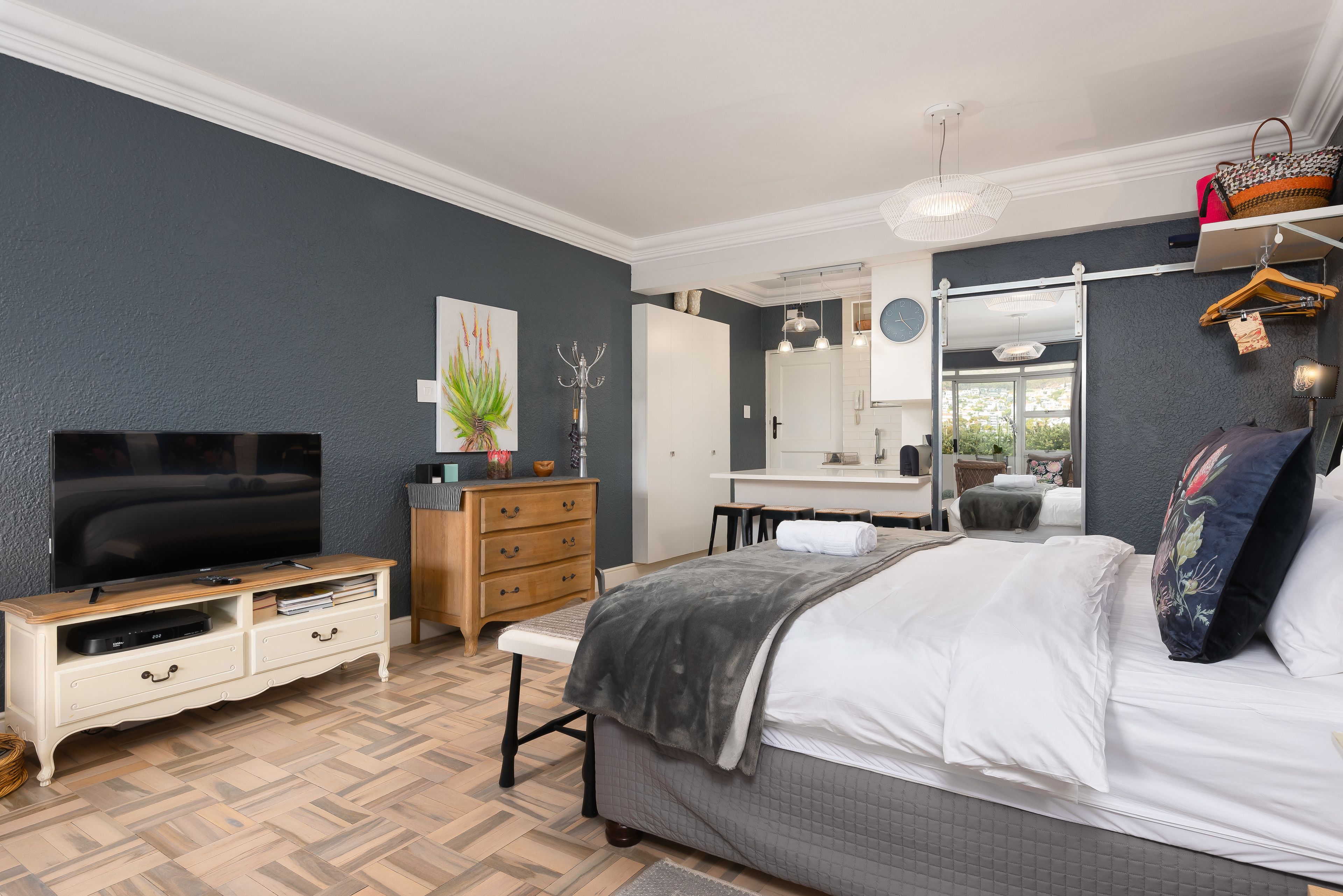 A modern bedroom with a large bed, a TV, a dresser, and a vanity.