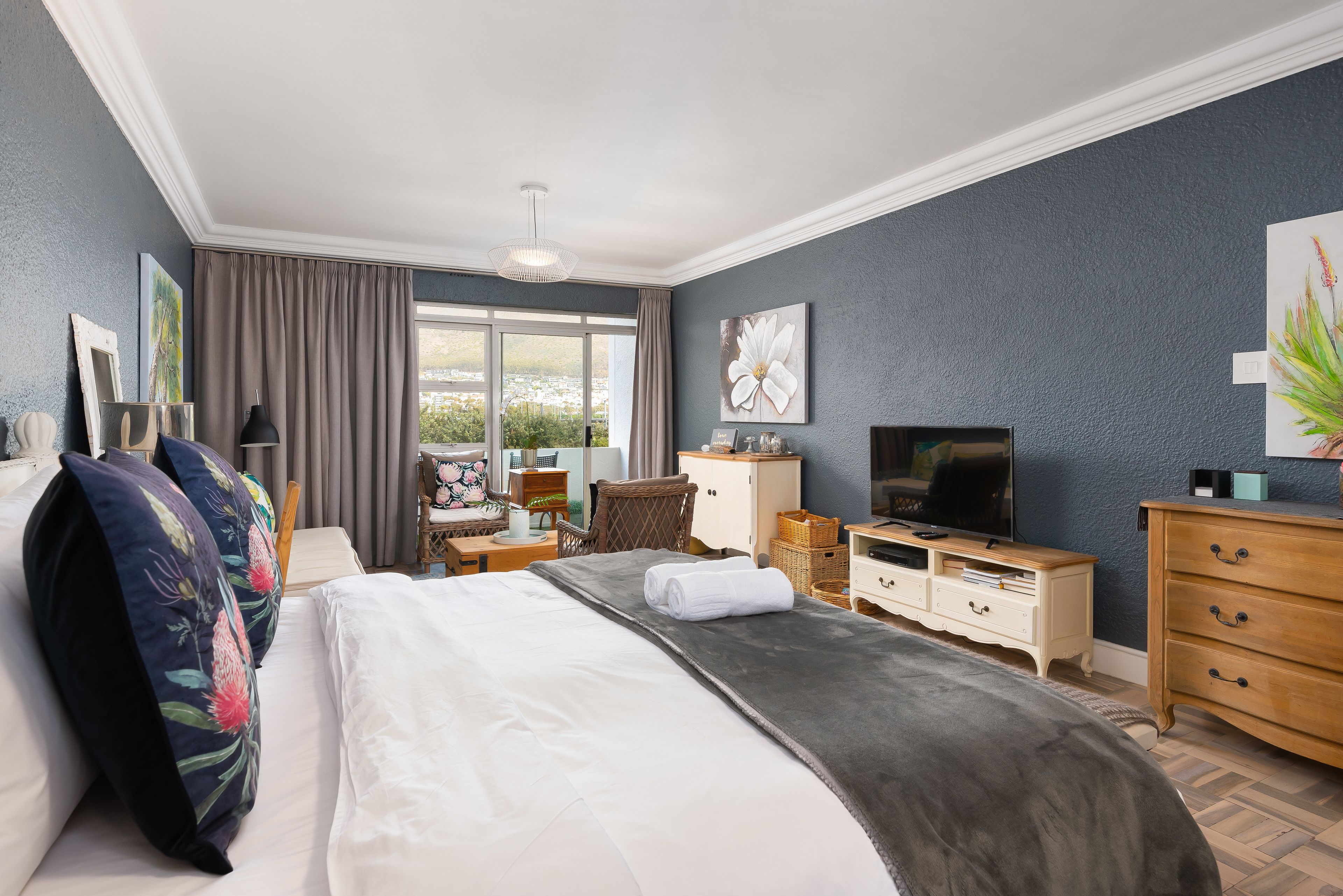 Ein Hotelzimmer mit einem großen Bett, einem Fernseher, einem Schminktisch und einem Fenster mit Vorhängen.